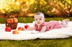 a baby laying on a blanket with apples in front of her and an apple basket