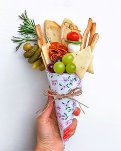 a hand holding an ice cream cone filled with cheese, crackers and olives