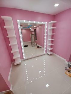 a pink room with white shelves and lights on the wall, and a large mirror in the corner