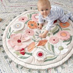 a baby is playing on a rug with flowers in the middle and leaves around it