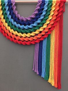 a multicolored crocheted scarf hanging on a wall next to a coat rack