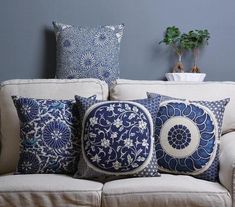 a couch with blue and white pillows sitting on it's backrest next to a potted plant