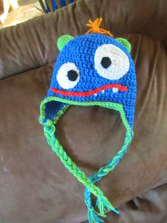 a blue crocheted hat with eyes on top of a brown leather couch in a living room