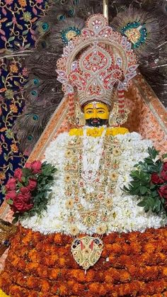 an idol sitting on top of a flower covered platform in front of a colorful wall