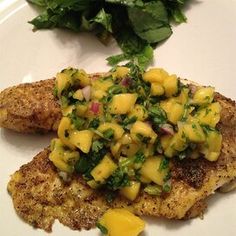 a white plate topped with chicken covered in mango salsa and green leafy greens next to a salad