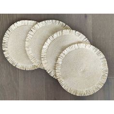 four white woven plates on a wood floor with fringes in the shape of circles