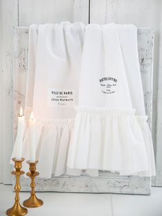 two candles are next to some white linens and one candle is on the table