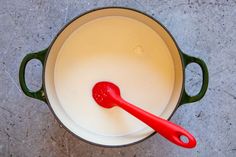 a red spoon sitting in a pot filled with milk