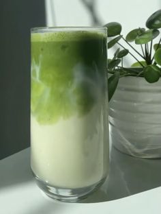 a glass filled with green liquid next to a potted plant