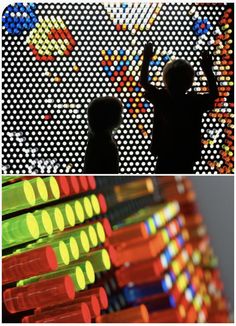 two children are standing in front of an array of colored lights, and one is holding his hand up