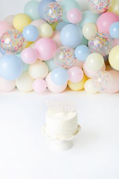 a white cake surrounded by balloons and confetti