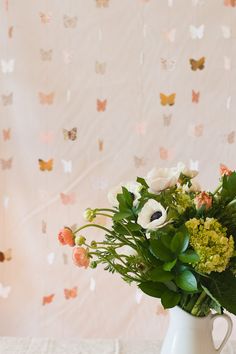 a white vase filled with flowers on top of a table next to a butterfly wallpaper