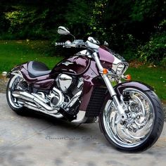 a purple motorcycle parked on top of a cement parking lot next to green grass and trees