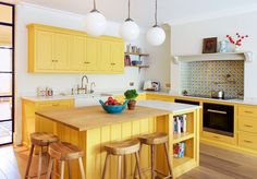 a bowl of fruit is on the island in this yellow kitchen with two stools