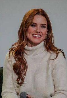 a woman with long hair sitting in front of a microphone and smiling at the camera