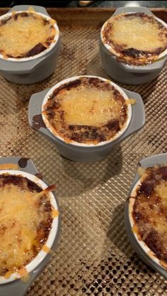 four casserole dishes sitting on top of a baking tray covered in cheese and sauce