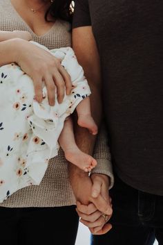 a man and woman holding the hand of a baby in their arms while standing next to each other