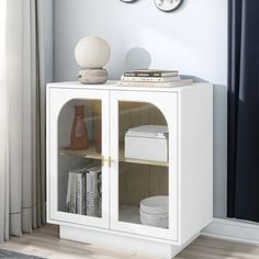 a white cabinet with two clocks on the wall above it and a book shelf below