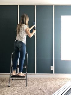 a woman is standing on a ladder and painting the walls