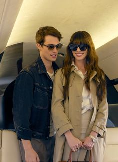 a man and woman standing next to each other on a white couch holding a brown purse