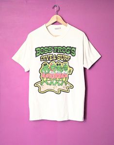 This shirt was made for the infamous 'Boss Frog's Surf & Dive' surf shop in Maui, Hawaii. Item is very lightweight, soft, breathable, and has that great retro style! This is a double-sided graphic shirt with awesome pictures of a group of cartoon frogs on the front and the back. Item is in great condition with no major holes, rips, stains, stress, or loose strings. Item has been pre-loved and it shows in the slight white fade. Size: M/M 19.5" wide from armpit to armpit 27.5" long from back of co Cartoon Frogs, Vintage White Shirt, Awesome Pictures, Maui Hawaii, Surf Shop, Graphic Shirt, Infamous, Frogs, Graphic Shirts