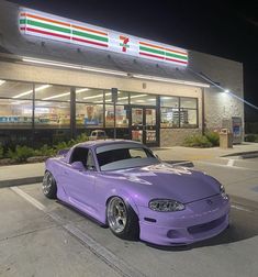 a purple sports car parked in front of a store at night with the lights on