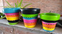 three colorful pots sitting on top of a brick wall next to a potted plant