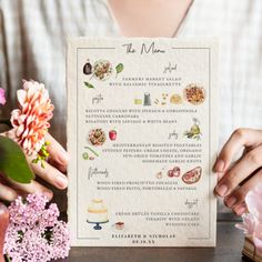 a person holding up a menu on top of a wooden table next to pink flowers