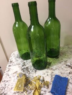 three green glass bottles sitting on top of a counter next to a blue sponge and cleaning cloth