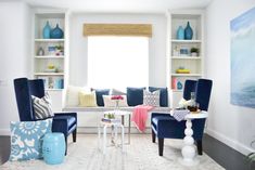 a living room filled with blue chairs and white shelves next to a window covered in bookshelves