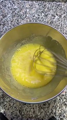 a metal bowl filled with yellow liquid and whisk