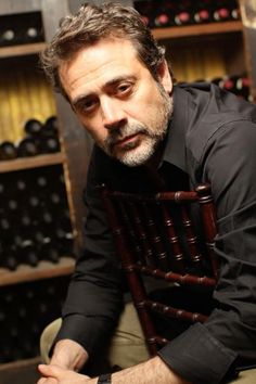 a man sitting in a chair next to a bunch of wine bottles on the shelves