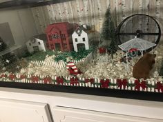 a display case with christmas decorations and fake animals in the front, behind it is a white picket fence