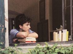 a young man leaning his head on a window sill with books in front of him