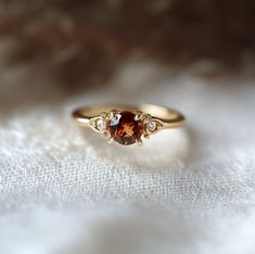 a close up of a gold ring with an orange stone in the middle and three diamonds on each side