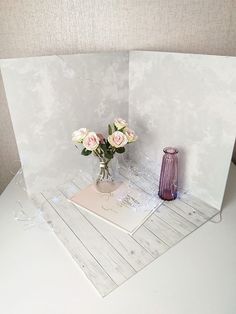 a vase filled with pink roses sitting on top of a white table next to a card