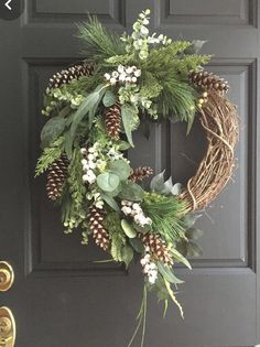 a wreath on the front door with pine cones and greenery