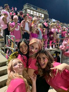 three girls in pink shirts posing for the camera at a sporting event with other people