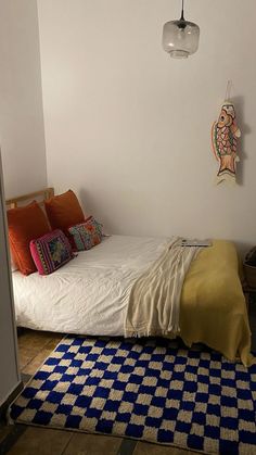 a bed sitting next to a white wall in a room with a blue and yellow rug