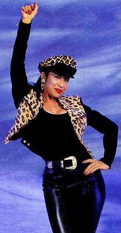 a woman in black pants and leopard print jacket with her hand up to the side