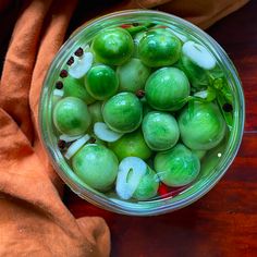 a glass bowl filled with green apples on top of a wooden table next to an orange towel