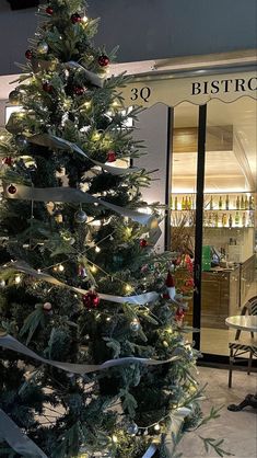 a christmas tree in front of a store with lights on it's branches and decorations