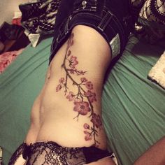 a woman laying on top of a bed next to a green sheet with flowers tattooed on it