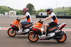 two people riding on the back of motorcycles down a race track in orange and black