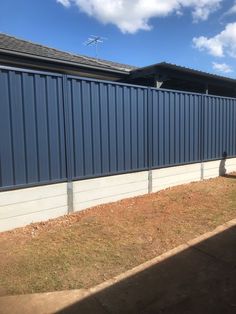 a blue metal fence in front of a house with grass on the ground and a building behind it