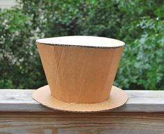 a brown paper cup sitting on top of a wooden table next to some green trees