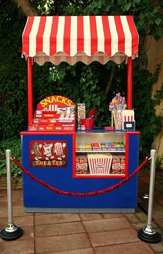 a red and white striped awning next to a blue stand with popcorn on it