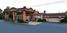 the front of a motel with an attached parking lot and covered in shrubs, bushes and trees