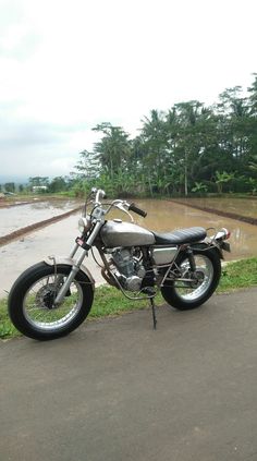 the motorcycle is parked on the side of the road by the rice paddocks