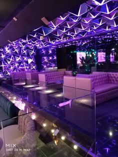 the interior of a nightclub with purple lighting and white couches, tables and chairs